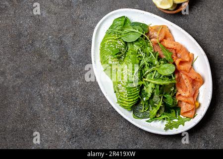 Bassa di un glucide insalata. Gli spinaci, rucola con insalata di avocado e salmone. Nero lo sfondo di calcestruzzo, piastra bianca, vista dall'alto Foto Stock