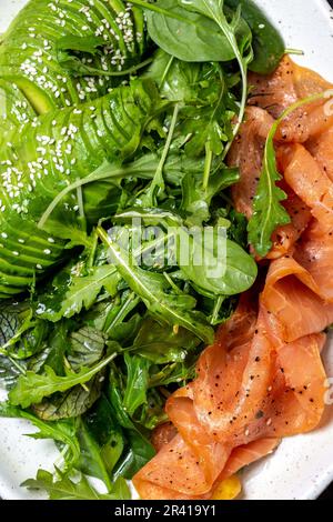 Bassa di un glucide insalata. Gli spinaci, rucola con insalata di avocado e salmone. Nero lo sfondo di calcestruzzo, piastra bianca, vista dall'alto Foto Stock