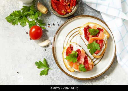 Panini aperti o bruschetta con salmone salato, formaggio e pomodoro essiccato al sole su un tavolo di pietra. Cibo sano, frutti di mare. Visualizza da Foto Stock