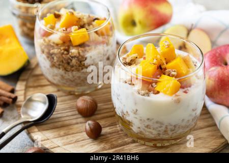 Sana colazione all'autunno o all'inverno al granola. Dessert fatto in casa con yogurt, muesli, mele al caramello e zucca, cannella, noci Foto Stock