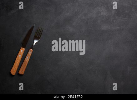 Forchetta e coltello con manico in legno su sfondo nero, vista dall'alto Foto Stock