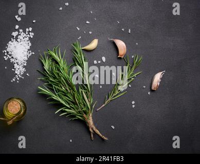 Sparso sale bianco grosso, pepe e rametti di rosmarino su un tavolo nero, ingredienti per cucinare pesce e carne Foto Stock