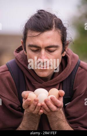 Felice giovane uomo Ritratto contadino tenendo le mani uova fresco Pollo biologico RawClose up galline ecologicamente coltivate in fienile di campagna agricola Foto Stock