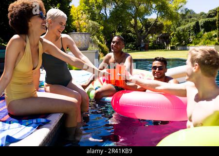 Felice gruppo variegato di amici che hanno partito in piscina, facendo brindisi in piscina in giardino Foto Stock