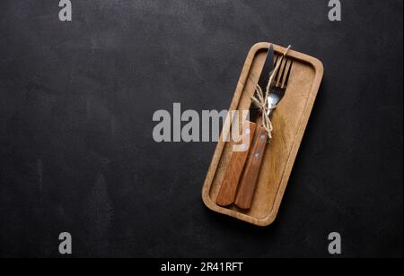 Forchetta e coltello con manico in legno su sfondo nero, vista dall'alto Foto Stock