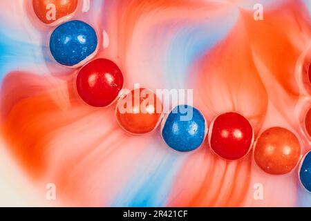 Effetto tie dye da arancione e rosso e blu skittle in acqua Foto Stock