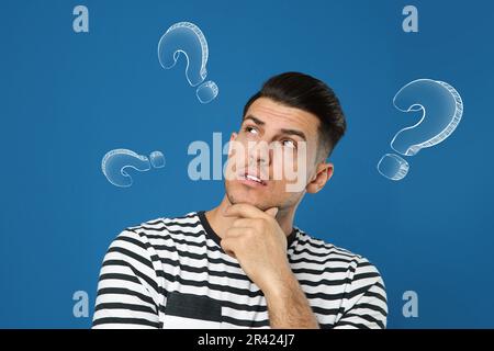 Scelta nella professione o in altri settori della vita, concetto. Prendere la decisione, uomo ponderato circondato da punti interrogativi disegnati su sfondo blu Foto Stock