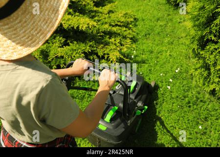 Donna che taglia erba con rasaerba in giardino nelle giornate di sole Foto Stock