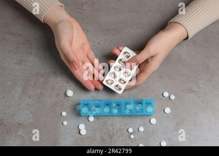 Donna che prende pillole da scatola di plastica al tavolo grigio, vista dall'alto Foto Stock