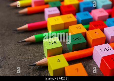 Molti cubi colorati con numeri, moltiplicazioni e matite su tavola grigio scuro, primo piano Foto Stock