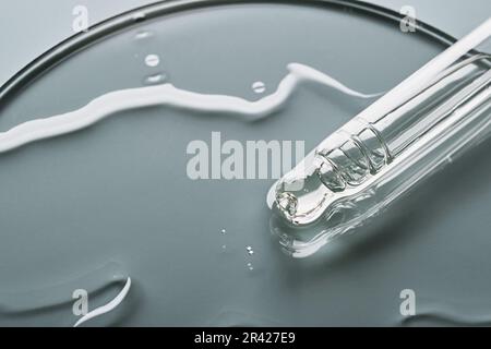 Pipetta con campione di prodotto cosmetico in capsula di Petri su sfondo grigio, messa a fuoco selettiva Foto Stock