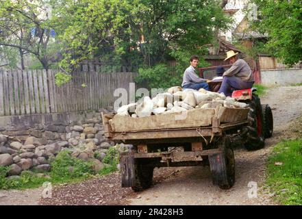 Maramures County, Romania, circa 2000. Trattore che trasporta su una corsia di un villaggio un rimorchio riempito di rocce del fiume. Foto Stock