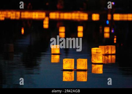 Lanterne dorate galleggiano su un tranquillo laghetto di notte con pareti di lanterne sullo sfondo Foto Stock