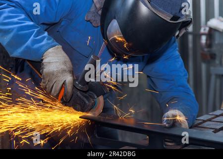 Durante la lavorazione dei metalli, i luoghi di lavoro in cui il maestro macina il metallo con la smerigliatrice sono visibili scintille in tutta la fabbrica durante il suo lavoro Foto Stock