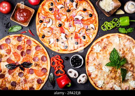 Selezione di diverse pizze su sfondo nero e ingredienti. Peperoni, pizza vegetariana e di pesce Foto Stock