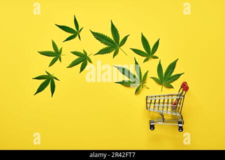 Carrello e foglie di marijuana su sfondo giallo. Concetto legale di cannabis Foto Stock