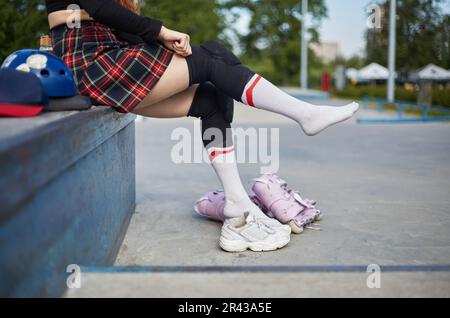 Roller blader ragazza mettere su ginocchiere di protezione prima di pattinare. Giovane skater femmina che si prepara per un giro in uno skatepark Foto Stock