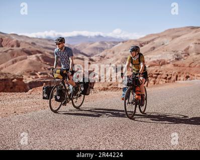 Due ciclisti pedalano lungo la remota strada di montagna nel deserto del Marocco Foto Stock