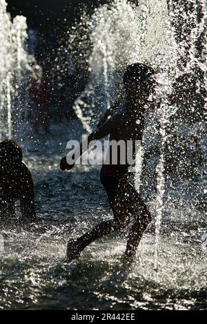 Silhouette di bambini che si raffreddano in una fontana durante l'onda di calore Foto Stock