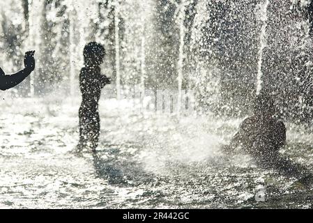 Silhouette di bambini che si raffreddano in una fontana durante l'onda di calore Foto Stock