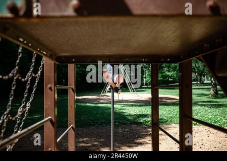 Immagine senza volto del bambino che si arrampica su palo su parco giochi in metallo a. Foto Stock