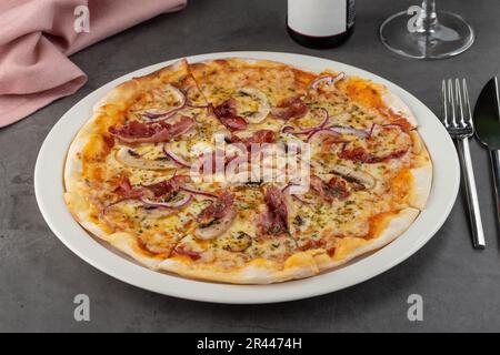 Pizza con pancetta e funghi su piatto di porcellana su tavolo di pietra Foto Stock