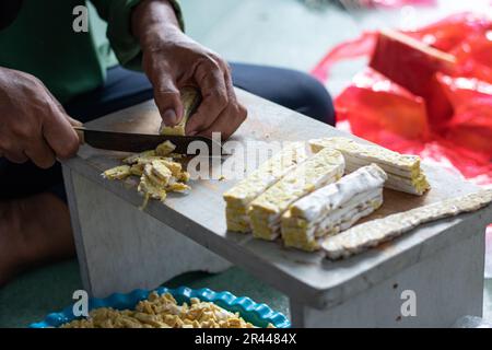 Donna asiatica che affetta tempeh crudo sul tavolo di legno usando un coltello. Tempeh o Tempe è un prodotto di soia fermentata originario dell’Indonesia Foto Stock