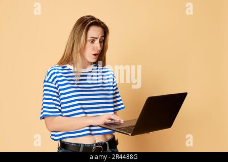 Ritratto di giovane ragazza in camicia a righe stilanding con laptop su sfondo giallo studio. Scadenze, sfide Foto Stock