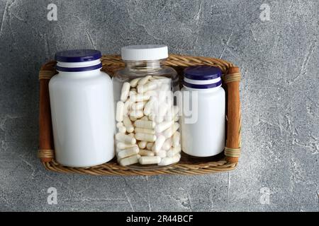 Flaconi medici con pillole in vassoio di vimini su tavolo testurizzato grigio chiaro, vista dall'alto Foto Stock