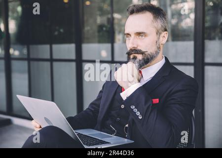 Uomo d'affari ispanico latino indiano adulto maschio baffi e barba pensiero intelligente con laptop seduto all'aperto Foto Stock