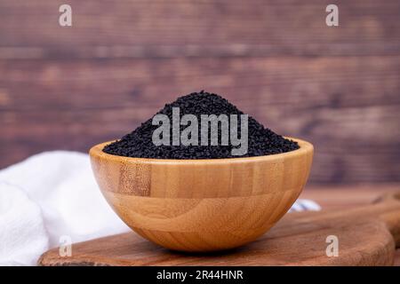 Cumino nero o nigella sativa su fondo di legno. Semi di cumino nero in ciotola di legno. Kalonji, nigella, cumino nero Foto Stock