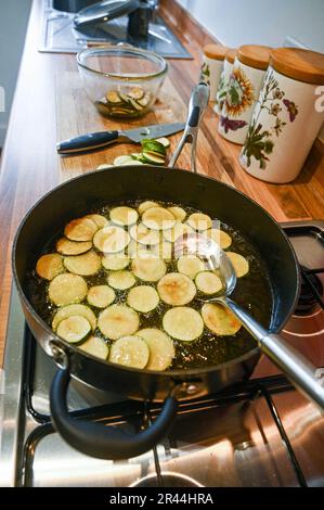 Friggere o rosolare le fette di zucchine o zucchine in olio di girasole pronte per l'uso in un piatto di pasta italiana Foto Stock