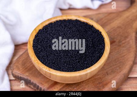 Cumino nero o nigella sativa su fondo di legno. Semi di cumino nero in ciotola di legno. Kalonji, nigella, cumino nero Foto Stock