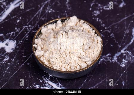 Polvere di aglio su fondo di legno. Spezie in polvere di aglio in polvere essiccate e macinate in un recipiente di legno Foto Stock