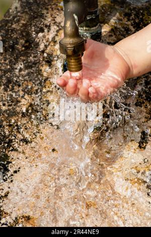 Il bambino pulisce le mani da un rubinetto esterno che esce da una pietra, spruzzi rinfrescanti senza sprecare acqua Foto Stock