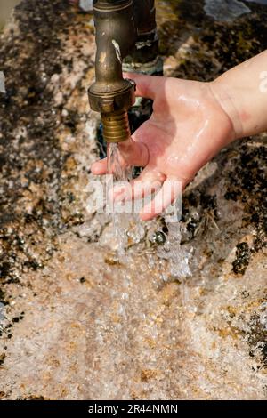 Il bambino pulisce le mani da un rubinetto esterno che esce da una pietra, spruzzi rinfrescanti senza sprecare acqua Foto Stock