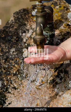 Il bambino pulisce le mani da un rubinetto esterno che esce da una pietra, spruzzi rinfrescanti senza sprecare acqua Foto Stock