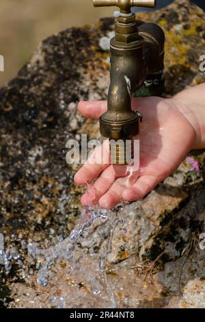 Il bambino pulisce le mani da un rubinetto esterno che esce da una pietra, spruzzi rinfrescanti senza sprecare acqua Foto Stock