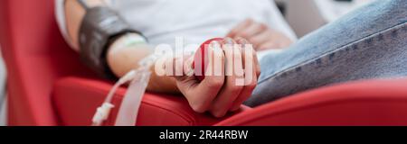 vista parziale del giovane volontario seduto su una comoda sedia ergonomica e schiacciando la palla di gomma durante la procedura medica nel centro di donazione di sangue, ba Foto Stock