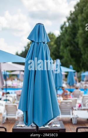 Ombrelloni ripiegati. Preparare la spiaggia per la nuova stagione di apertura. Ci sono molti ombrelloni accanto alla piscina. Il concetto di vacanza turistica Foto Stock