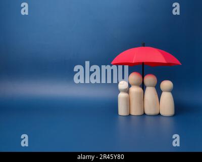 Quattro figurine giocattolo di legno contro l'ombrello rosso in miniatura contro una parete blu - spazio copia Foto Stock
