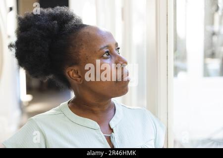 Donna afroamericana premurosa che guarda fuori dalla finestra a casa Foto Stock