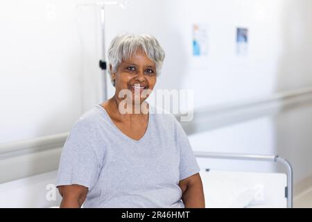 Ritratto inalterato di felice paziente anziana biraciale sul letto di ospedale sorridente, con spazio copia Foto Stock