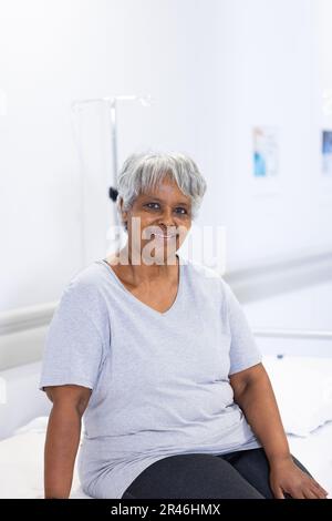 Ritratto inalterato di felice paziente anziana biraciale sul letto di ospedale sorridente, con spazio copia Foto Stock