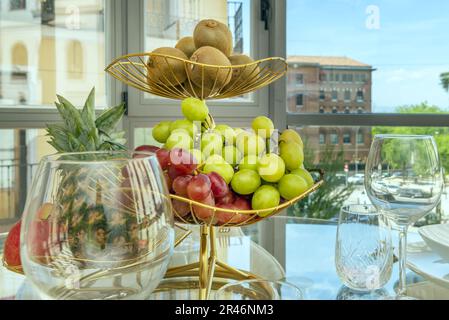 Una ciotola di frutta dorata con uva rossa e bianca, kiwi maturi e un ananas Foto Stock