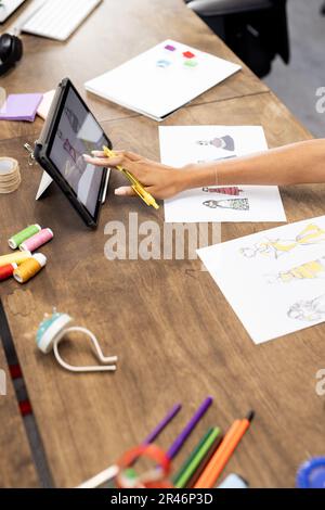 Biracial donna fashion designer realizzare progetti di moda con tablet in ufficio creativo, inalterato Foto Stock