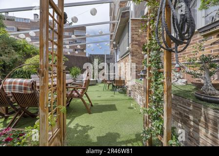 Terrazza di una casa con pavimenti in erba artificiale, tavoli, posti a sedere all'aperto, un sacco di piante e una tenda retrattile al piano terra di una casa Foto Stock