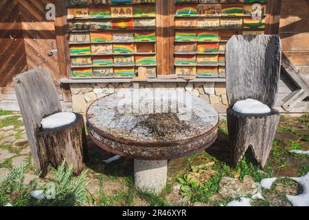 tavolo in pietra e sedie scolpite da tronchi d'albero nei pressi di un villaggio alpino Foto Stock