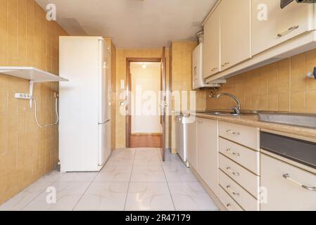 Una cucina dotata di vecchi armadi color crema, nuove piastrelle marroni sulle pareti e un piano di lavoro in legno Foto Stock