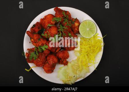 Un piatto bianco ripieno di ali di pollo e spaghetti su sfondo nero Foto Stock